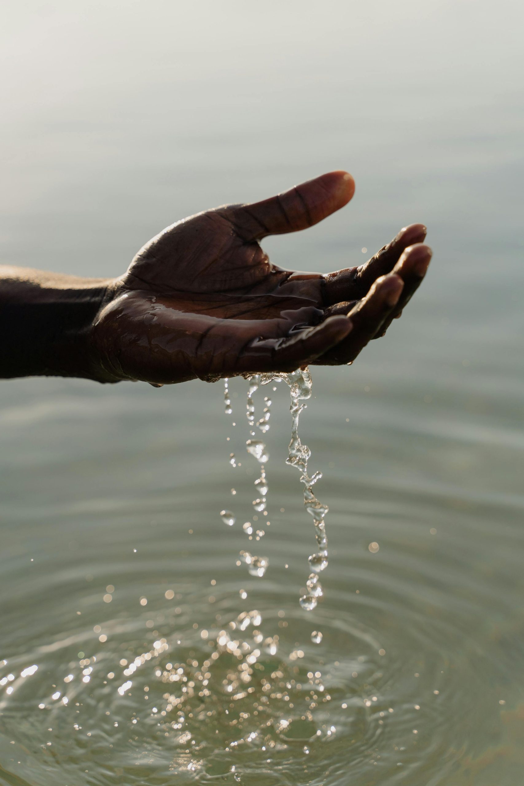 A close-up of a hand with water droplets falling outdoors, reflecting serenity and nature.